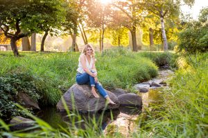 senior portrait sitting on rock in creek during golden hour outside